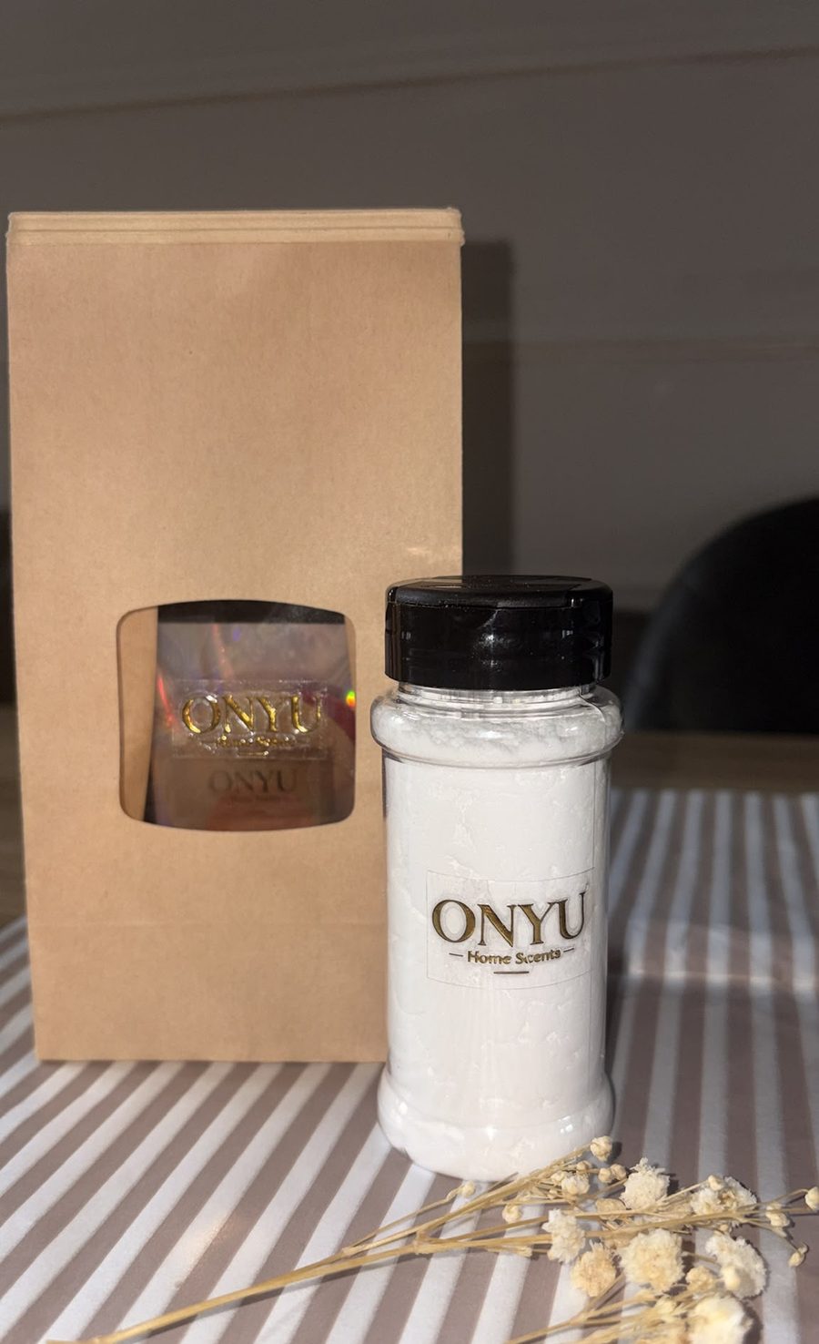 ONYU room spray bottle beside a kraft bag of scent sachets on striped linen